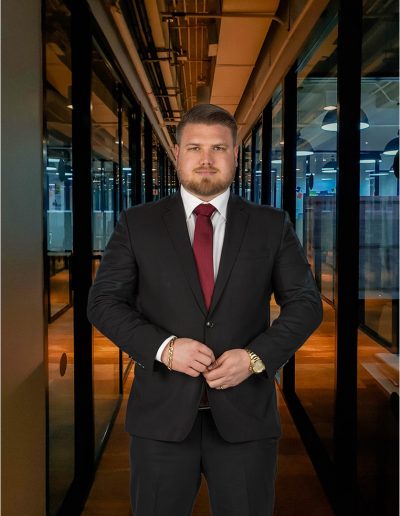 "A business man posing for shoot in a black suit with a red tie."