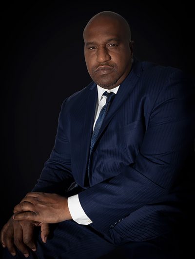 "A man in a dark blue suit sitting posing for headshot."